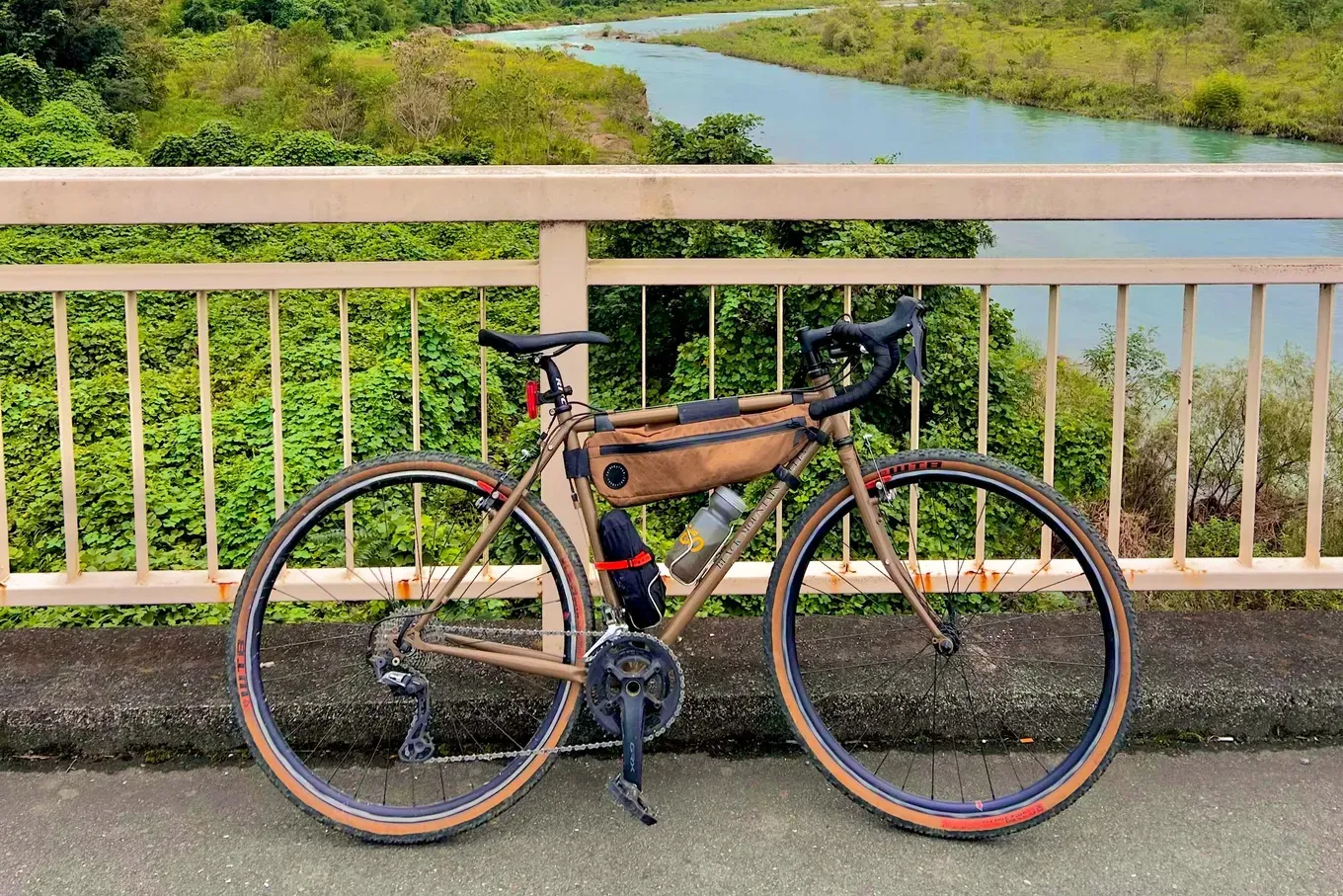 秋川にかかる橋の欄干の前に停めたグラベルロードバイク。奥に川と緑の山